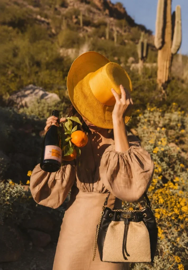 Woman in a desert landscape wearing the black bucket bag by Monica Zuccheri with natural raffia panels and gold chain strap