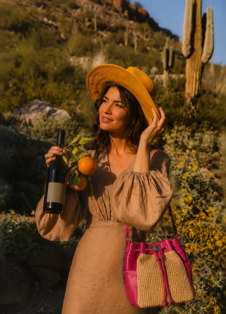 Woman in a linen dress carrying the Pink Valentino bucket bag by Monica Zuccheri on her shoulder among cacti and orange trees