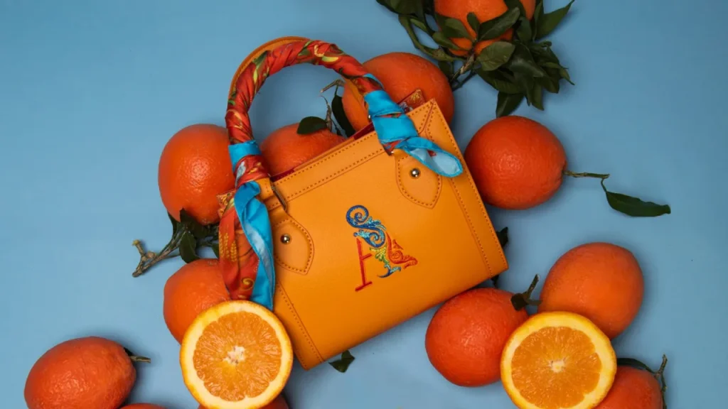 Close-up of the Mini Bag by Ammia showing the embroidered A monogram, gold-tone hardware and the printed silk scarf on the handle